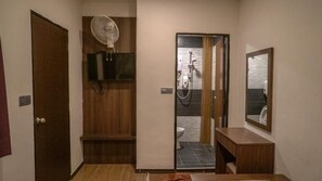 A bathroom with a shower, a fan, a mirror, and a wooden vanity.