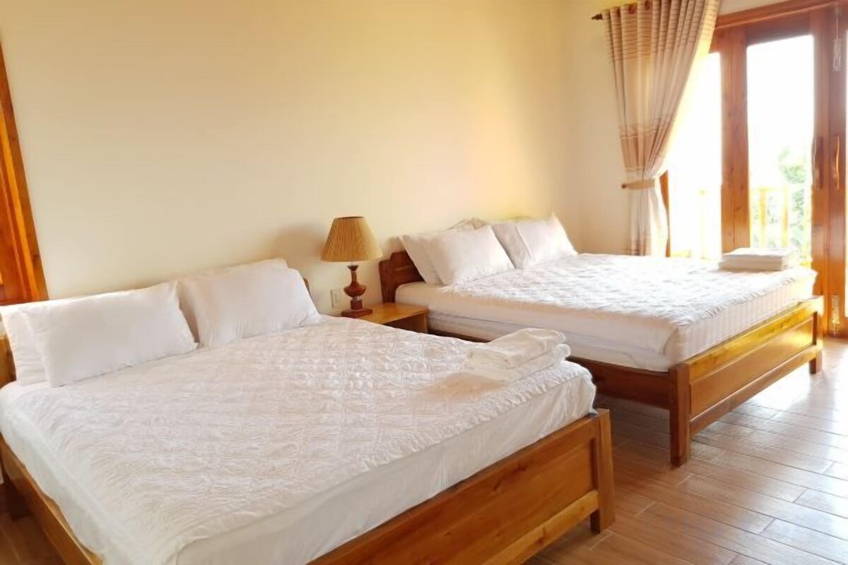 Two wooden beds with white bedding in a room with wooden flooring and a window with curtains.