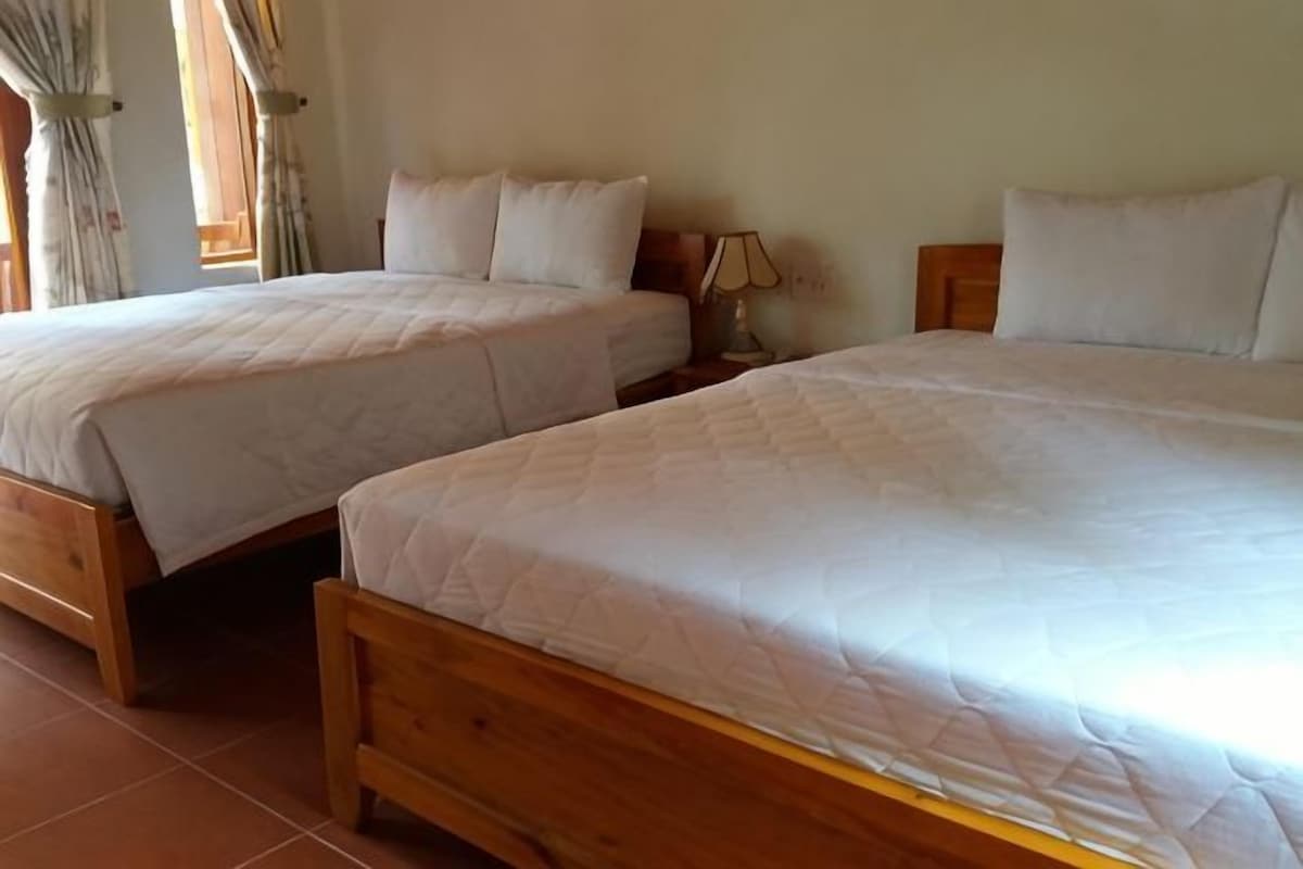 Two wooden beds with white bedding in a room with a tiled floor and a nightstand with a lamp.