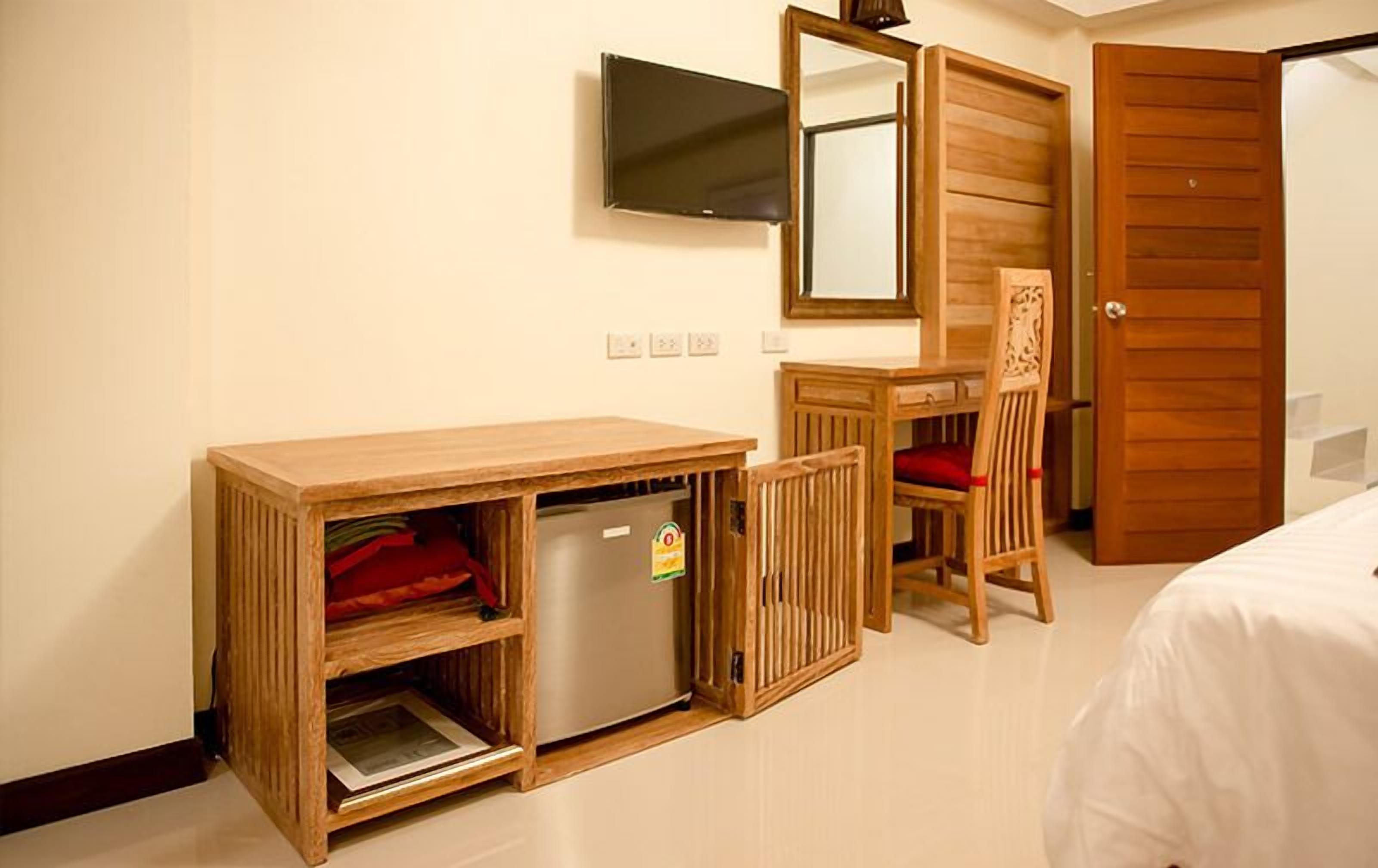 A compact hotel room with a wooden desk, a small refrigerator, a television mounted on the wall, a wooden chair, and a bed.