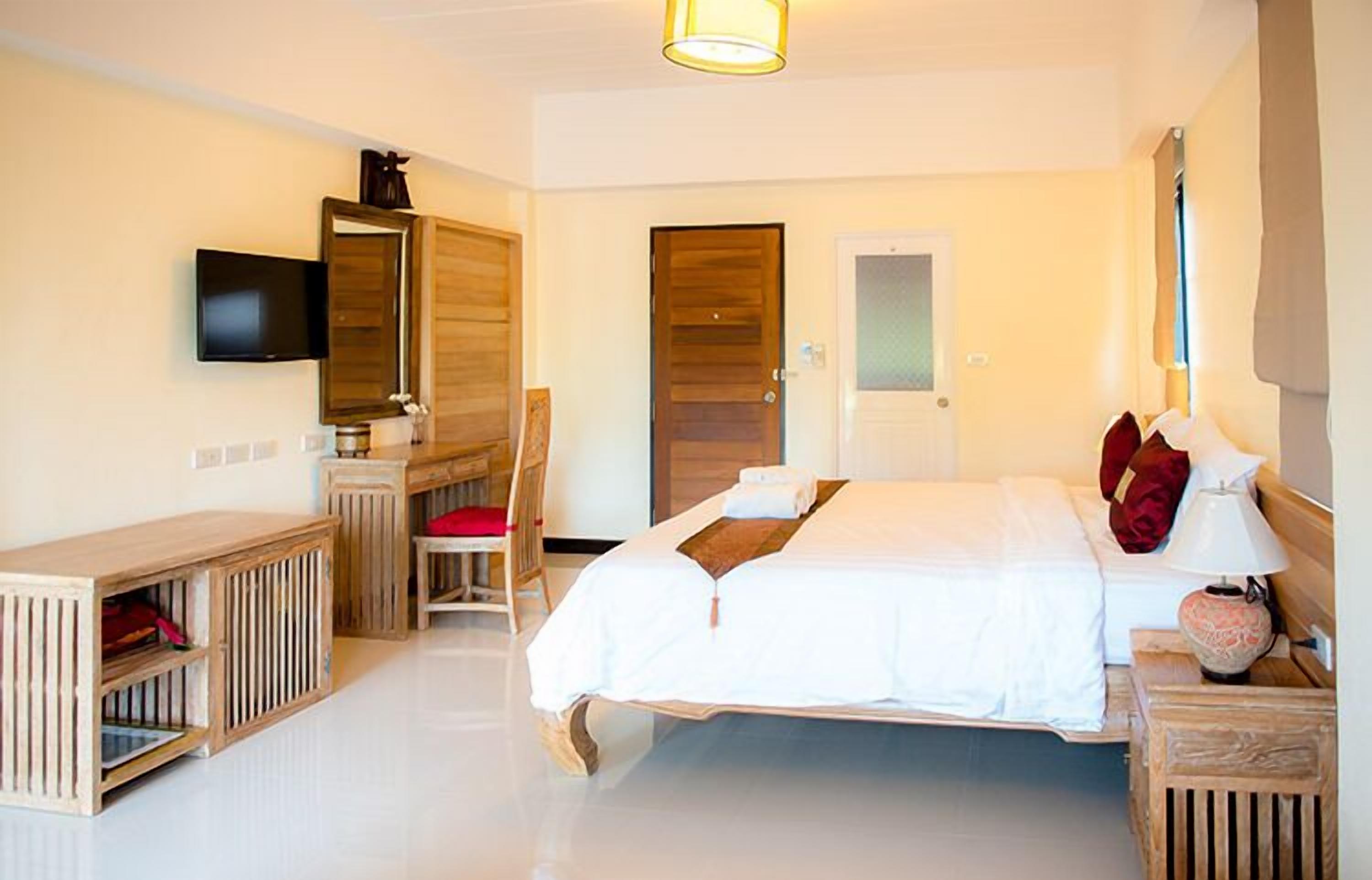 A bedroom with a bed, a desk, a chair, a television, and a door.