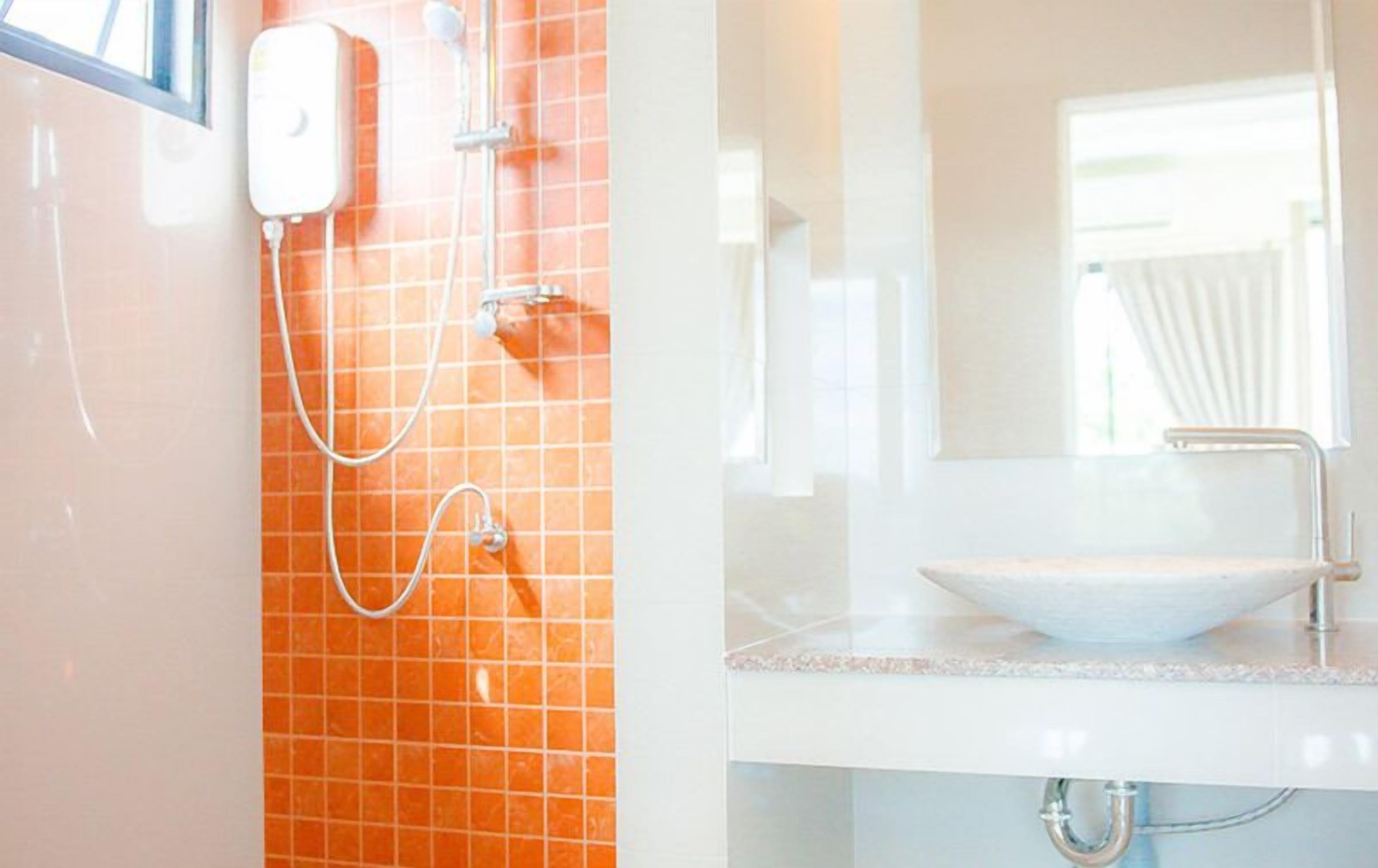 Un baño con un lavamanos blanco, cabina de ducha con mampara de vidrio y paredes con azulejos naranjas.