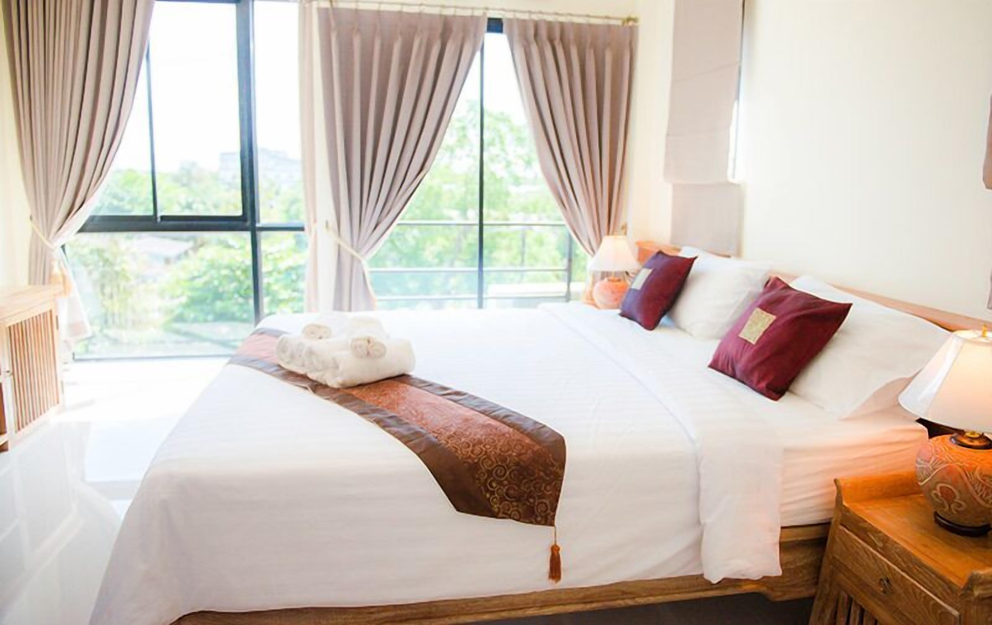 Un lit bien fait, avec des draps blancs, un plaid marron et deux coussins décoratifs.