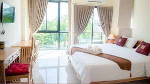 Habitación de hotel con una cama grande, un escritorio y una silla. Hay una ventana con cortinas, un equipo de aire acondicionado y un televisor montado en la pared.