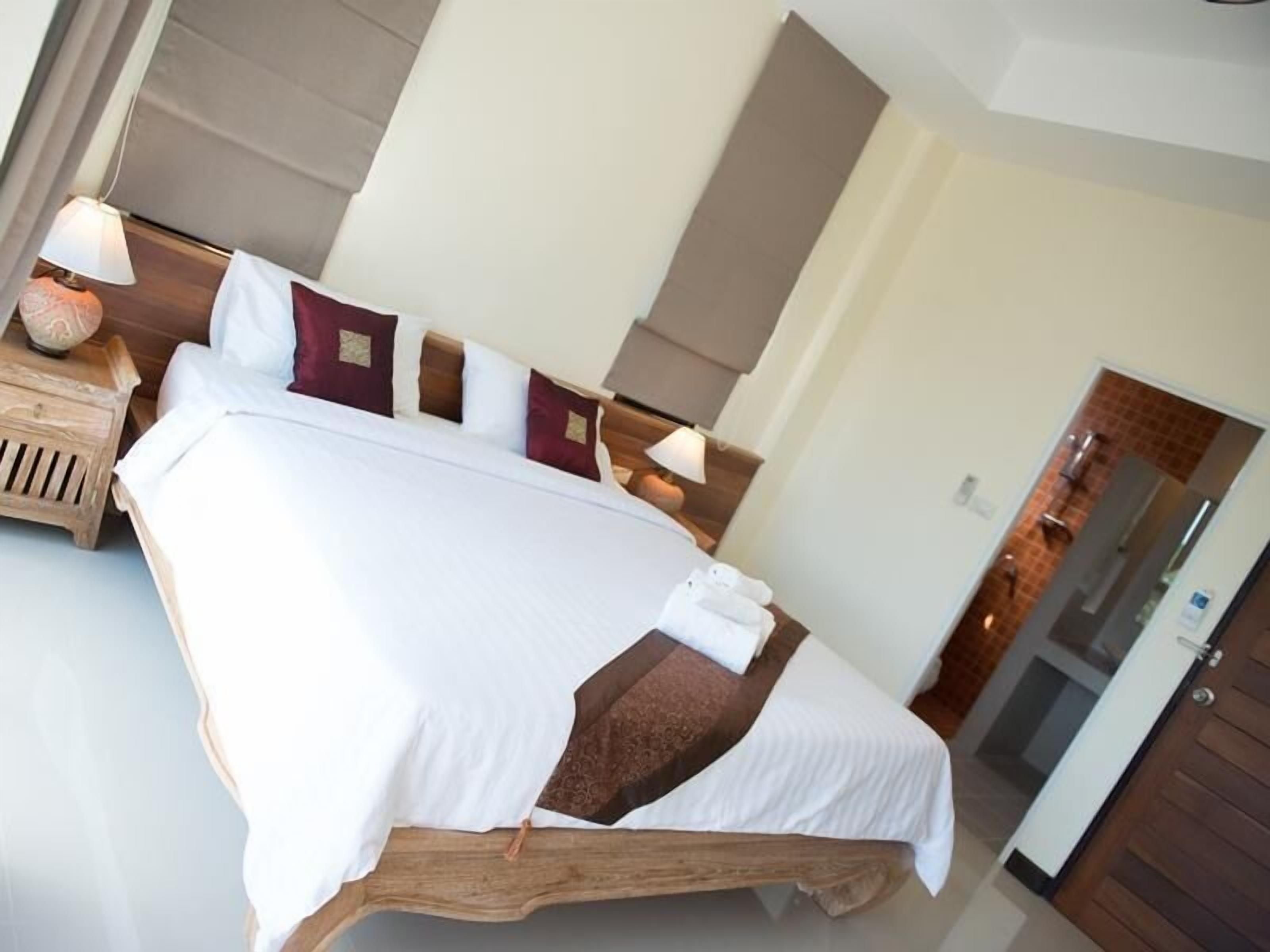 A neatly made bed with white and brown linens, a wooden headboard, and a bedside table with a lamp and a decorative item.