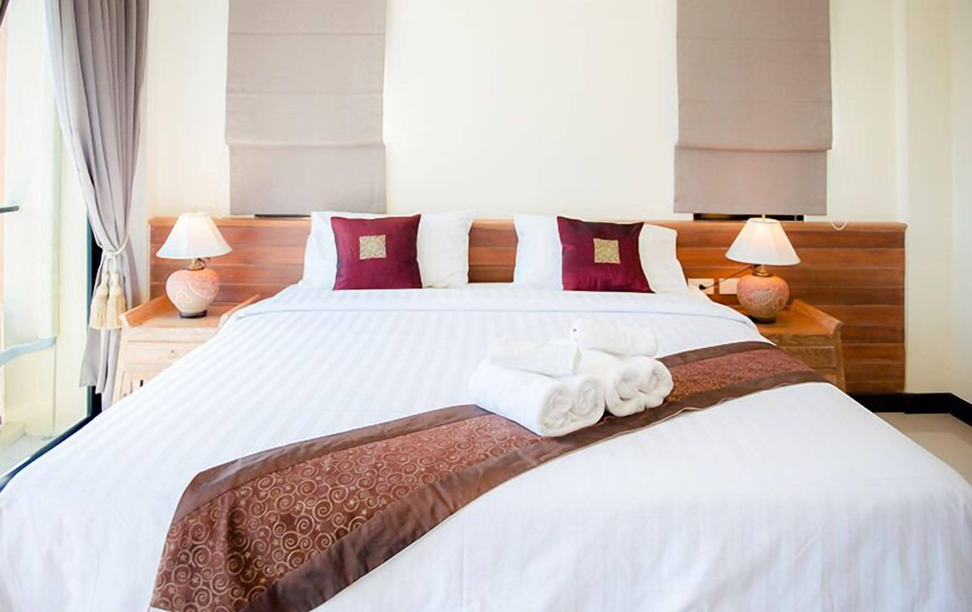 A hotel room with a large bed, two bedside tables with lamps, and a window with curtains.