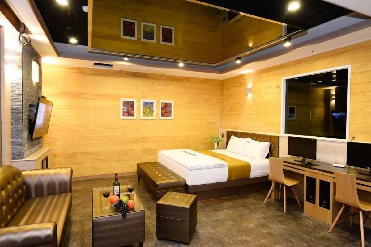 A modern hotel room with a bed, a desk, a sofa, and a television.