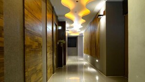 A modern hotel corridor with a glossy tiled floor, wooden panel walls, and a unique ceiling light fixture.