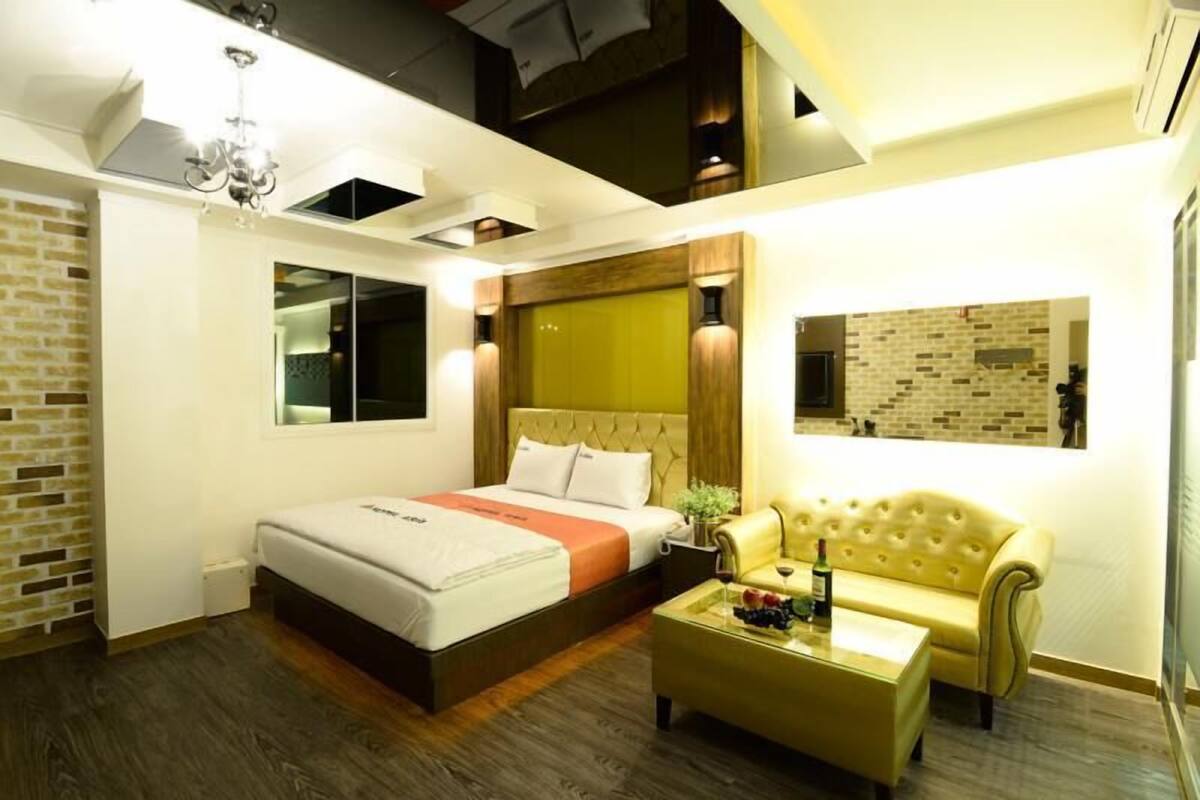 A modern hotel room with a large bed, a sofa, a coffee table, and a brick accent wall.