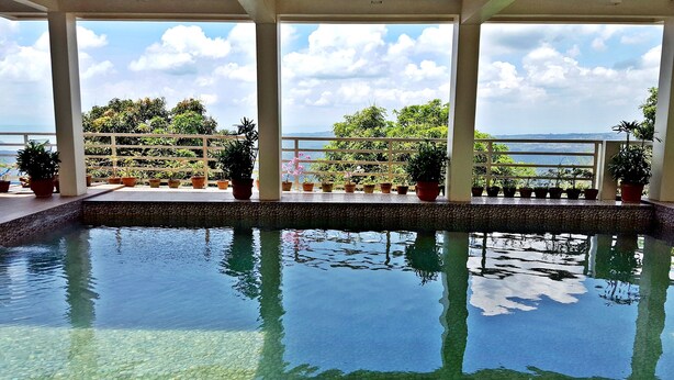 An indoor pool with clear water, surrounded by potted plants and a view of the sea. - Splash Suites Hotel Tagaytay (Tagaytay)