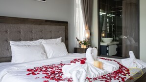 A hotel room with a large bed, a headboard, a bedside table with a bottle and flowers, and a bathroom visible through a glass door. - Hong Mon Resort Da Lat (Xuan Huong - Da Lat)