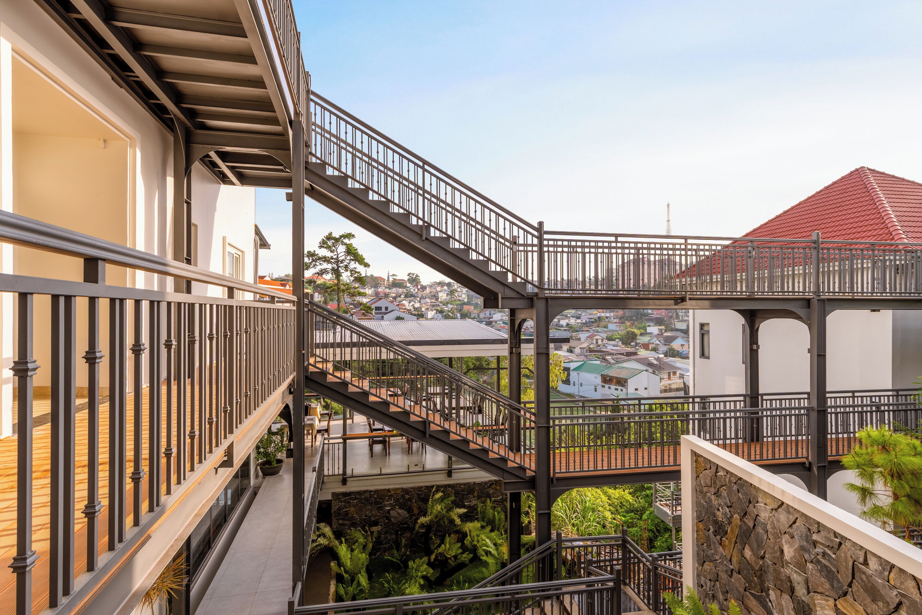 A multi-level outdoor balcony with metal railings, a stone wall, and a view of a residential area.