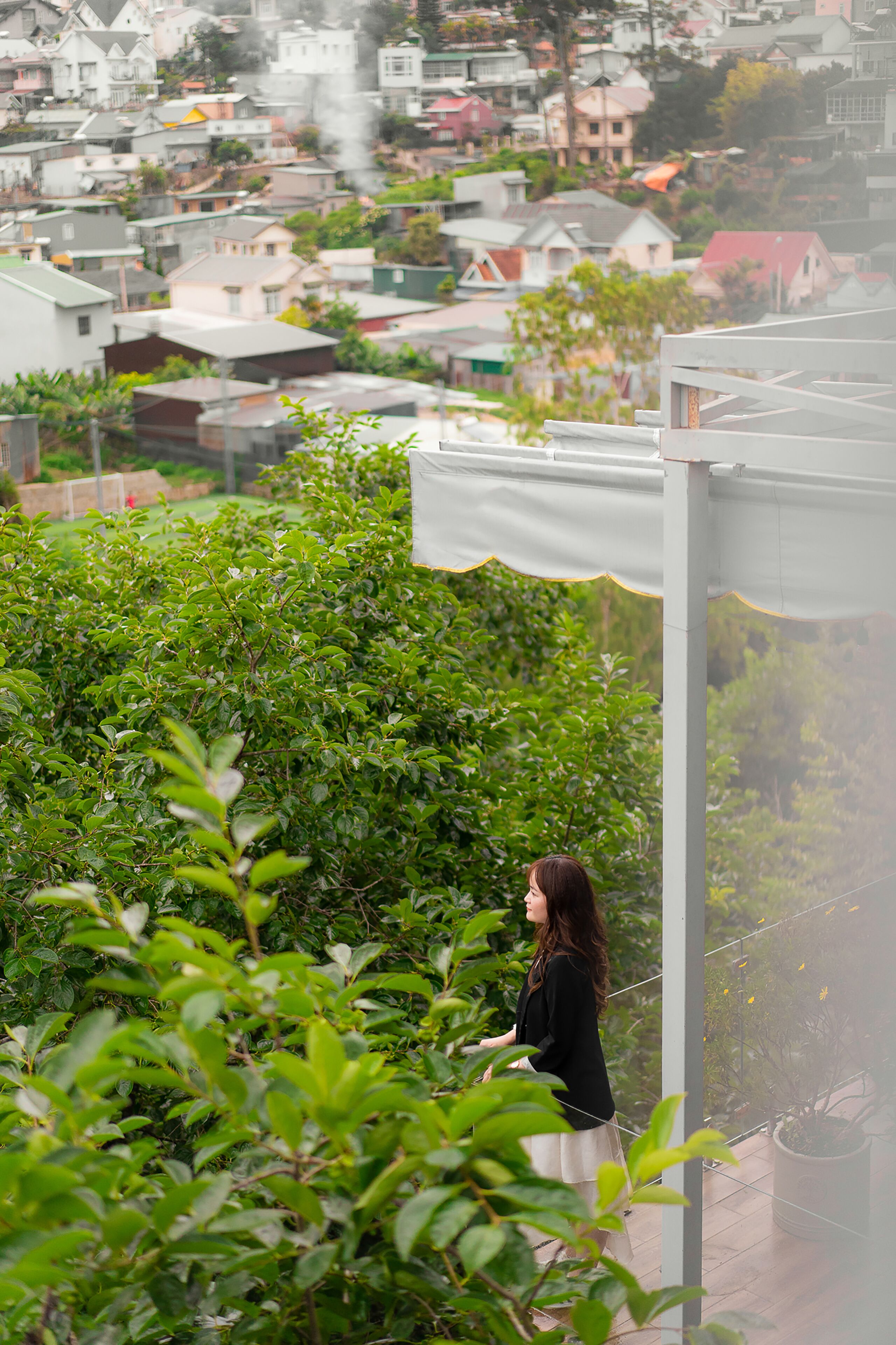 Une personne se tient sur un balcon donnant sur un quartier résidentiel, avec des maisons et de la verdure.