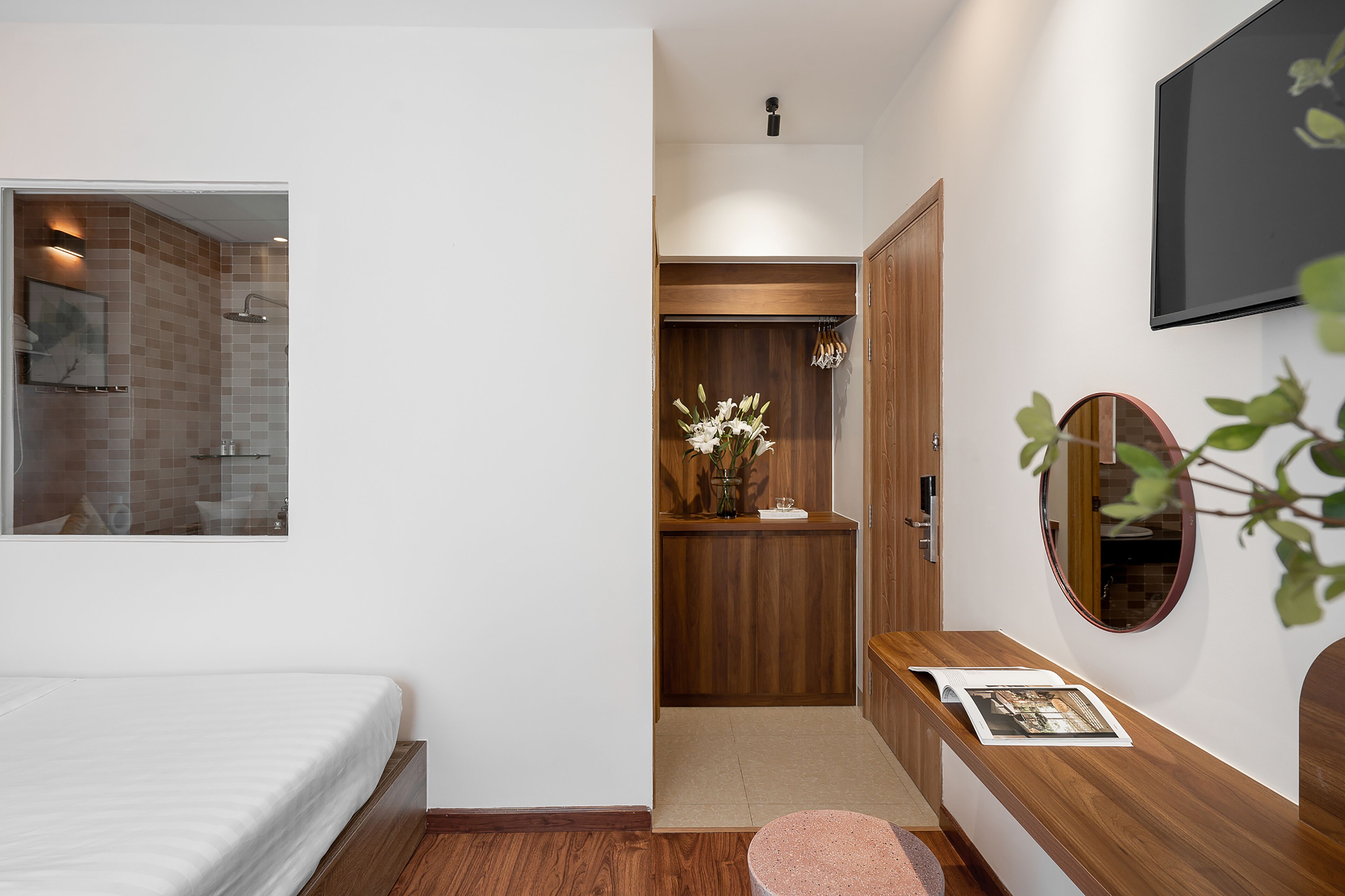 A bedroom with a bed, a wooden desk, a mirror, and a shower area.