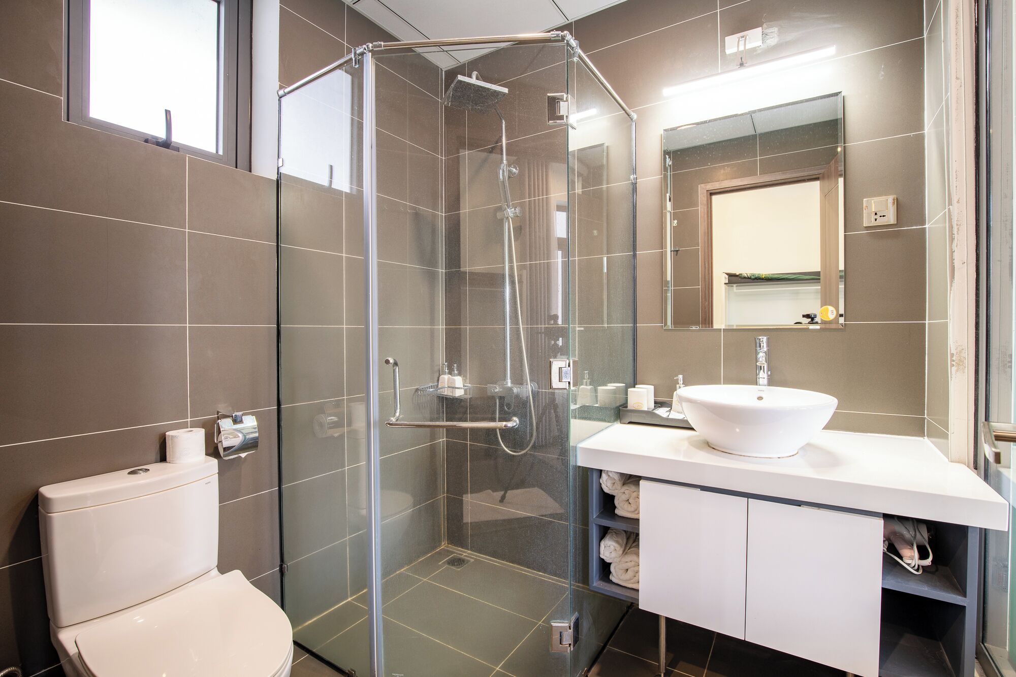 A modern bathroom with a glass-enclosed shower, a white sink, and a toilet.