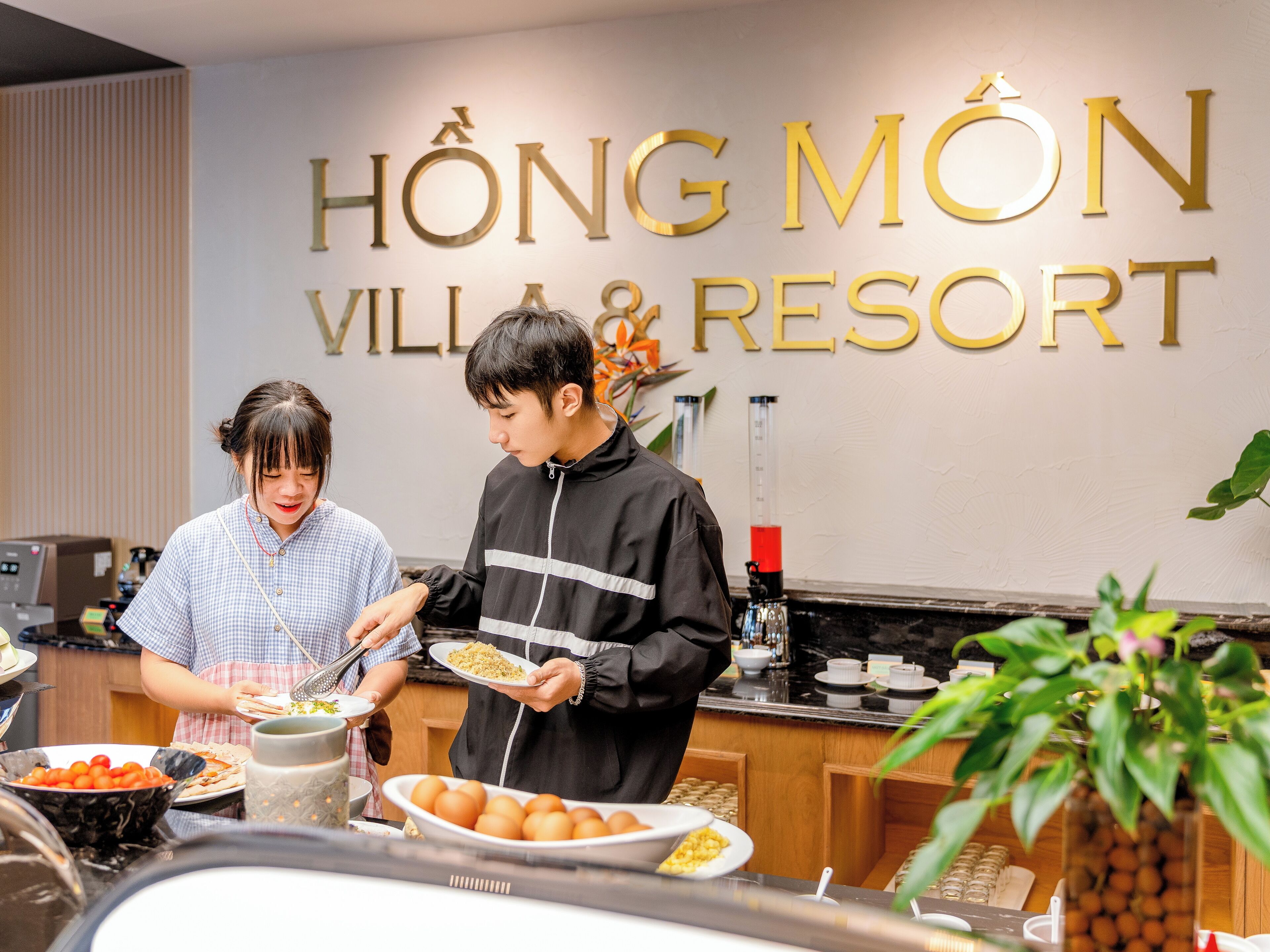 A buffet setup with various food items and a sign for HONG MON VILLA & RESORT in the background.
