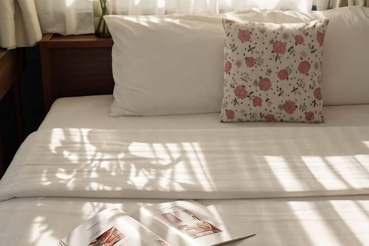 A bed with a white bedspread, a pillow with a floral pattern, and a magazine on the bed.
