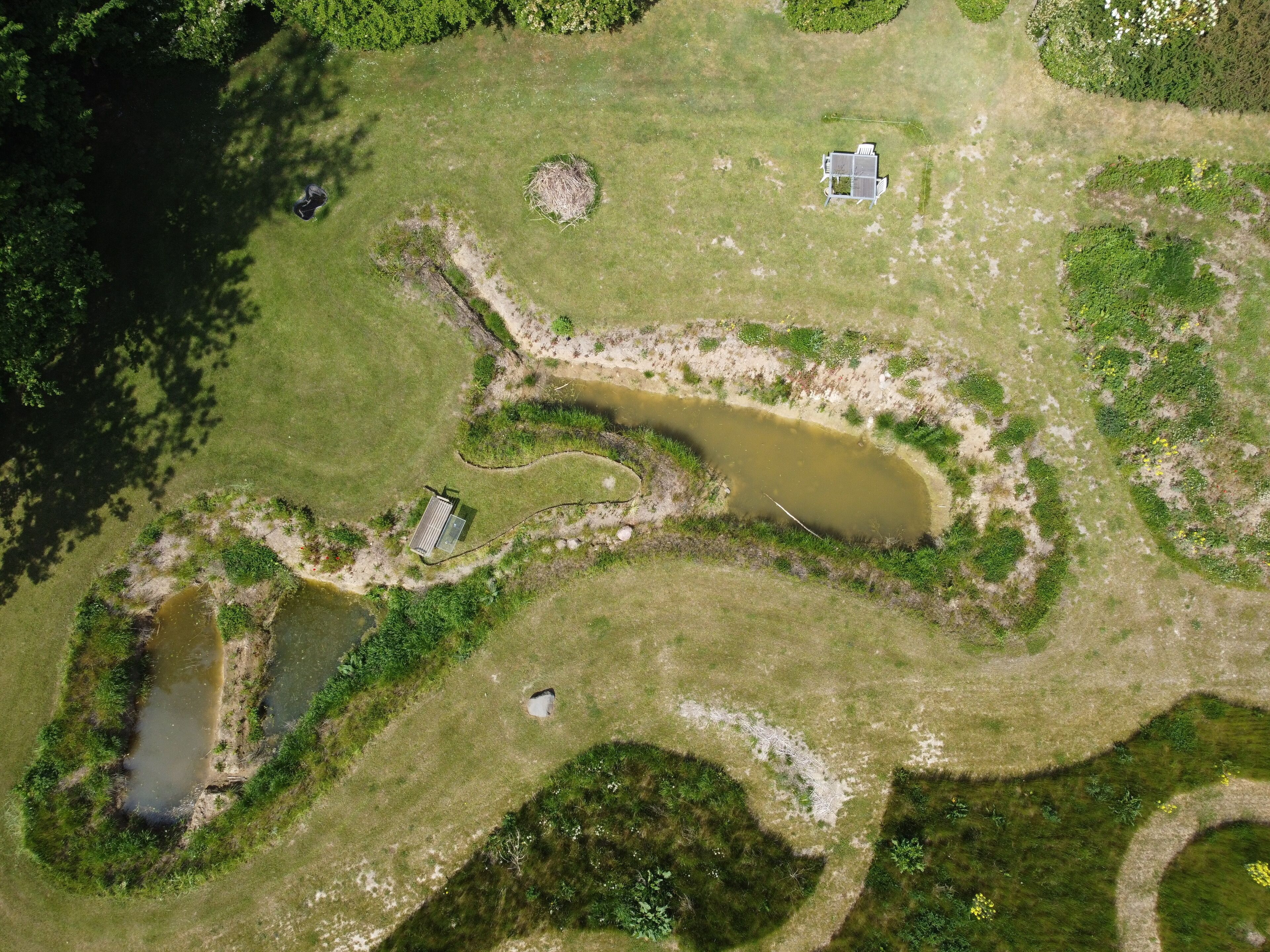 An aerial view of a property with a pond, a small building, and a fenced area.