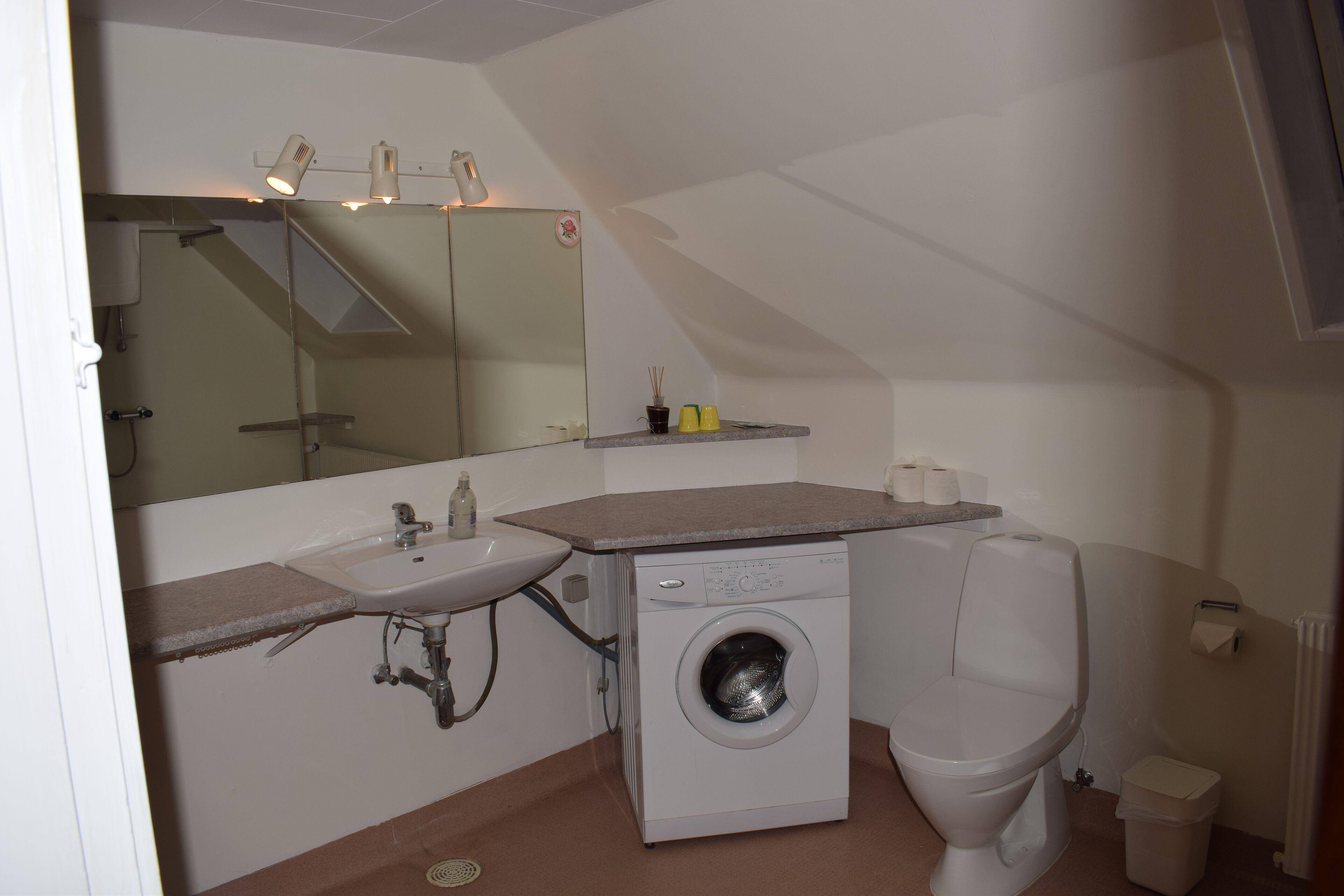 A compact bathroom with a sink, washing machine, toilet, and a mirror.