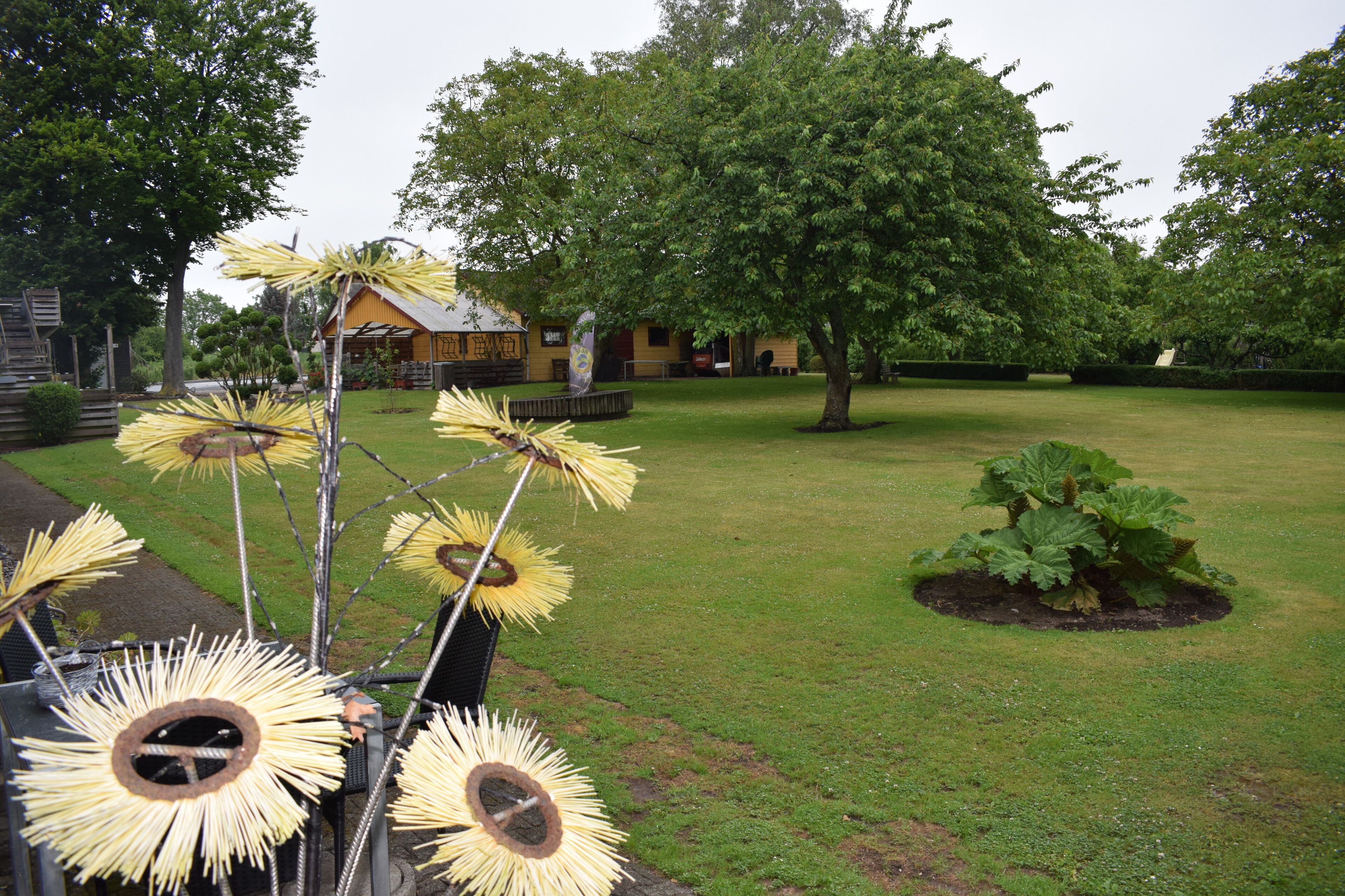 A grassy area with a decorative sunflower sculpture, a small garden, and a building in the background.
