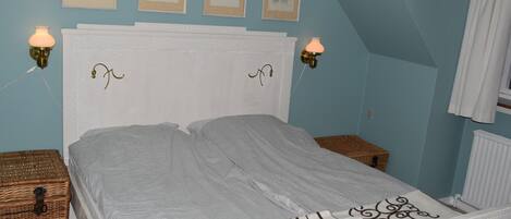 A bedroom with a white headboard, two bedside tables, a bed with a striped bedspread, and wall-mounted sconces.