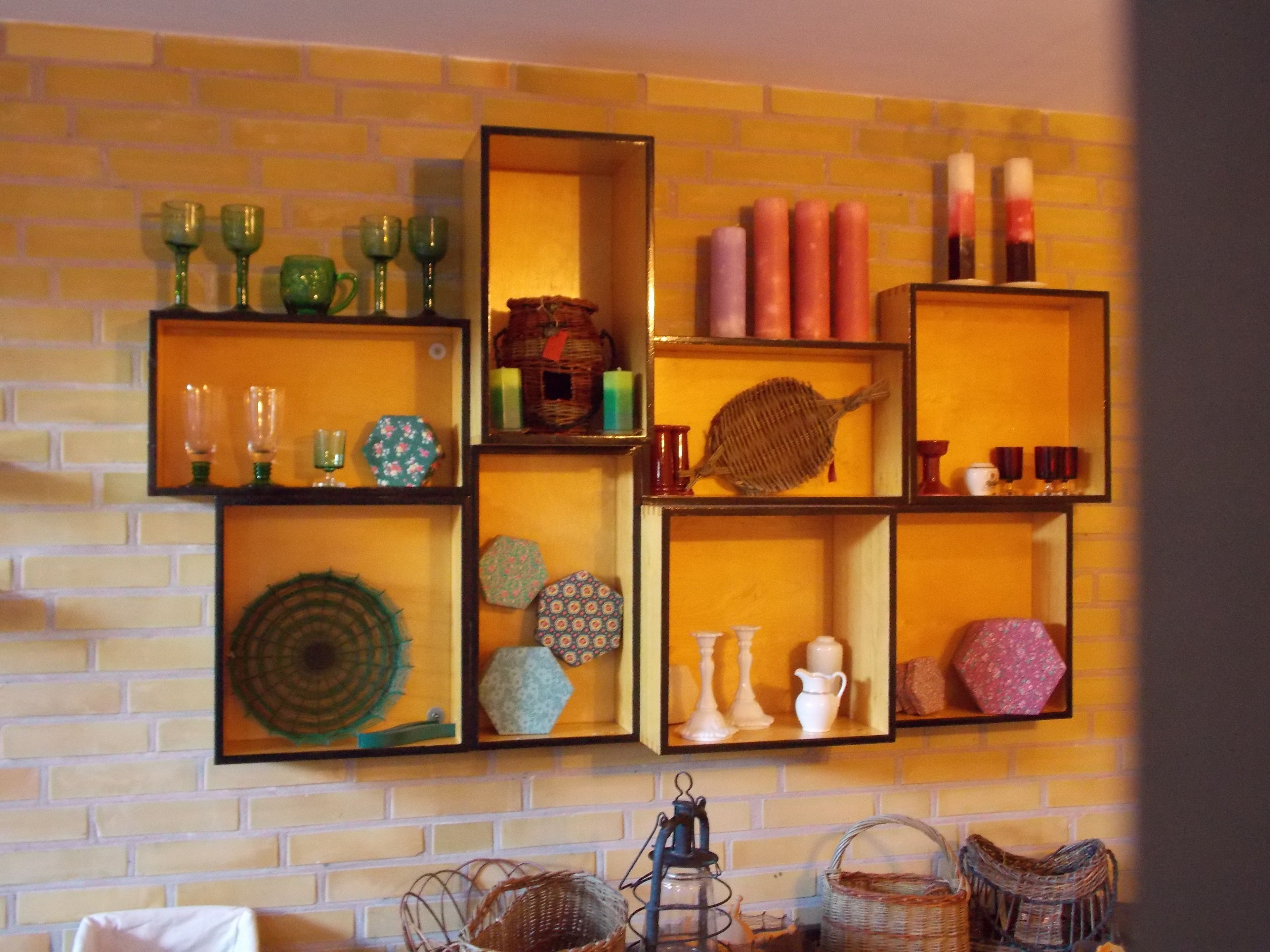 Een muur met meerdere planken waarop decoratieve objecten staan, zoals glaswerk, kaarsen en aardewerk.