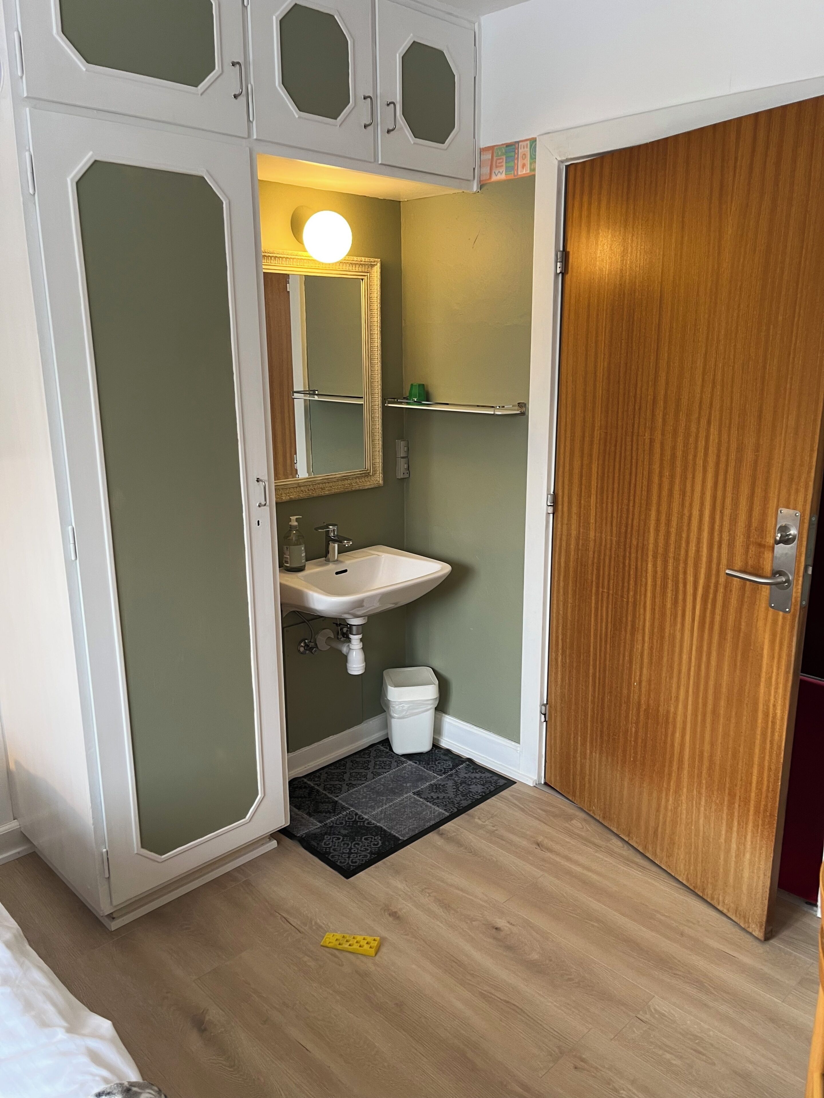 Un baño con lavamanos blanco, espejo, inodoro y puerta de madera.