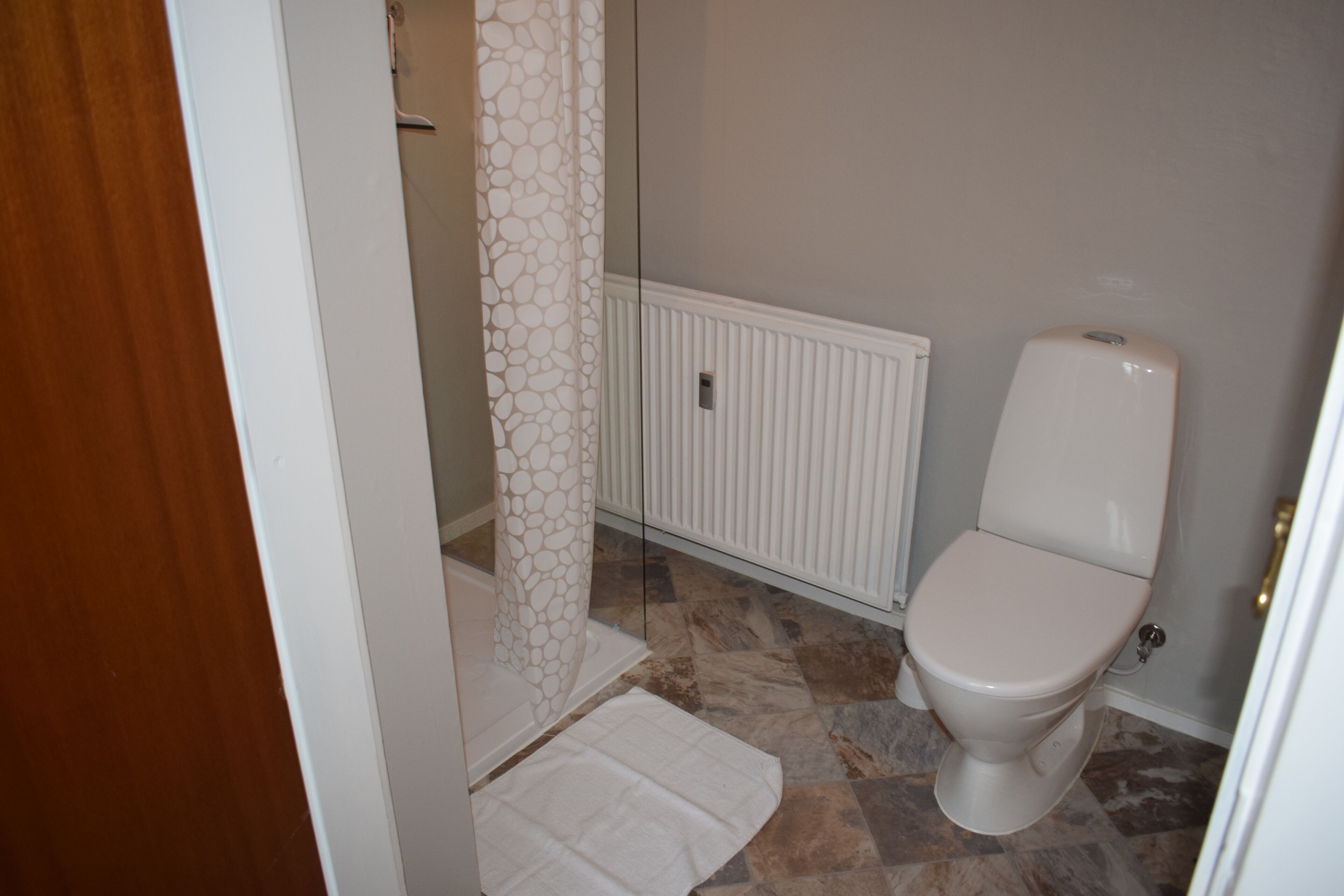 A bathroom with a toilet, a shower curtain, and a radiator.