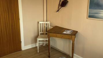 A bedroom with a bed, a wooden table, a chair, a radiator, a door, and a wall decoration.