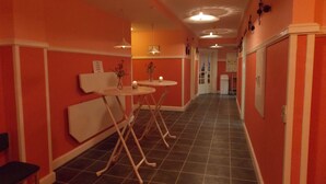 Ein Korridor mit orangefarbenen Wänden, einem gefliesten Boden und einer weißen Bank. Zwei runde Tische mit Kerzen und Vasen sind zu sehen.