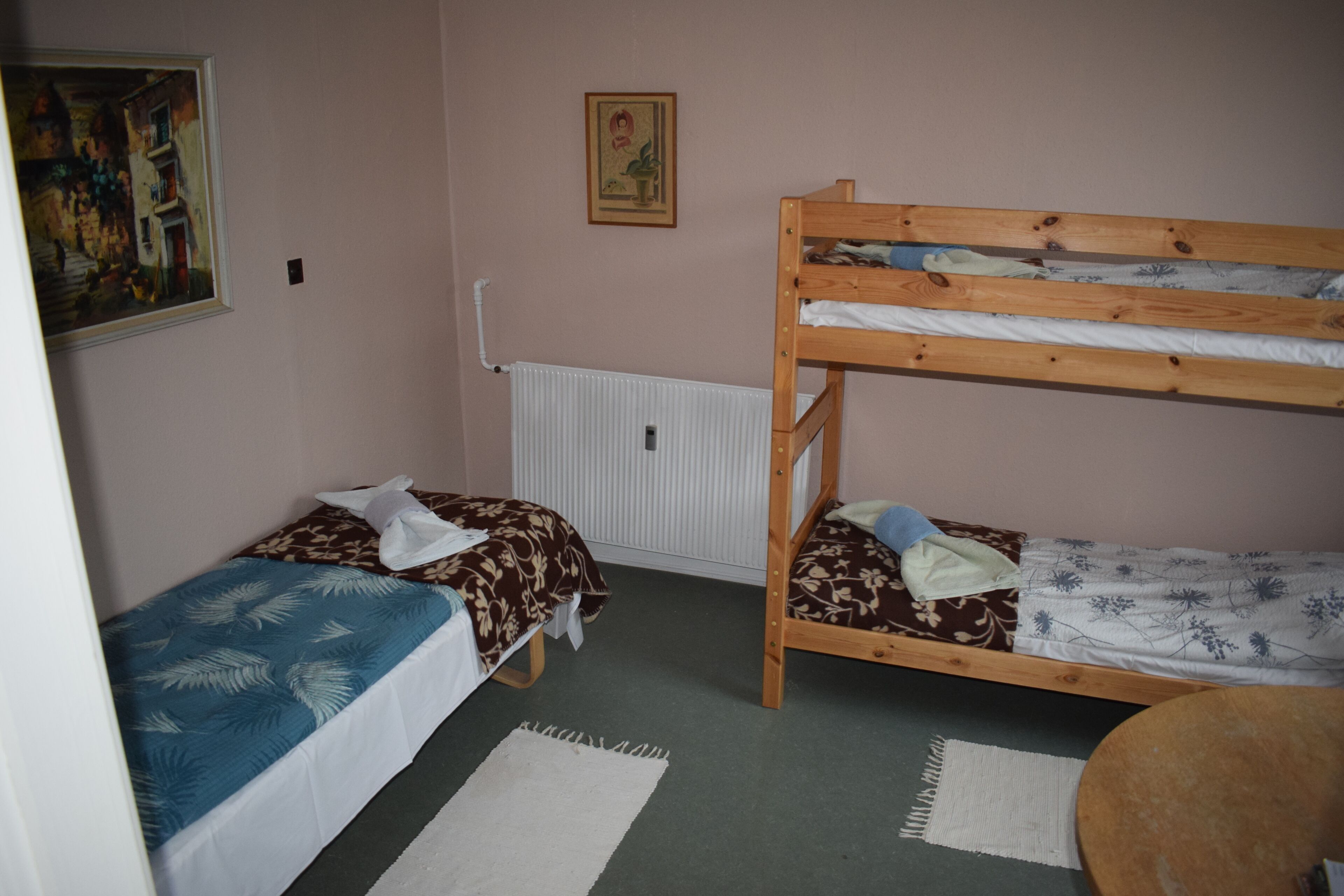 A room with two bunk beds, a radiator, a painting on the wall, and a small round table.