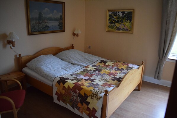 A bedroom with a wooden bed, a red chair, and two paintings on the wall.