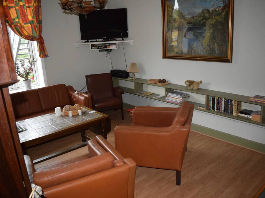 Una sala de estar con televisión, un cuadro, una estantería y muebles de cuero.
