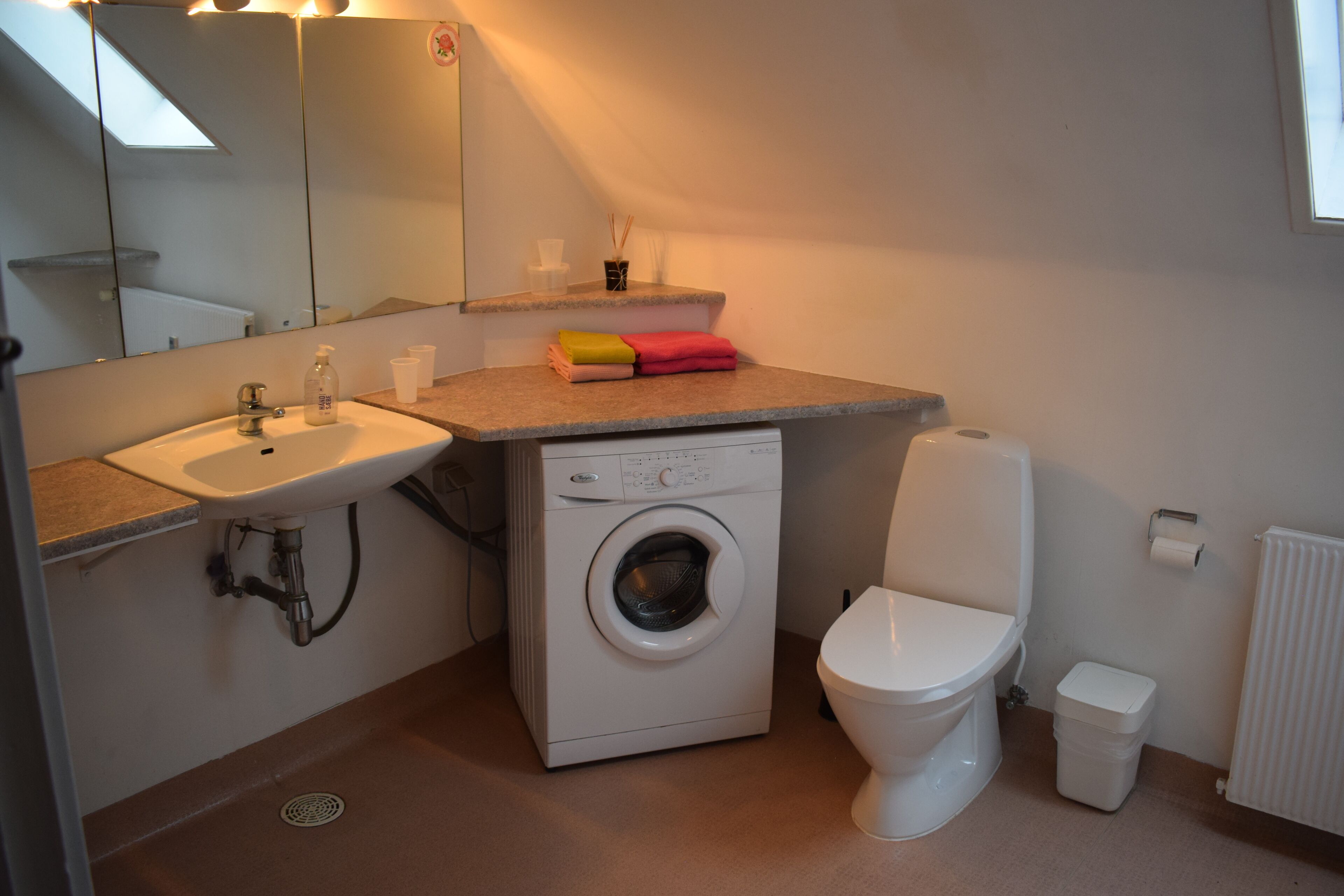 A compact bathroom with a sink, washing machine, toilet, and a mirror.