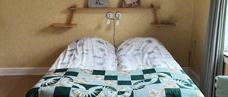 A bed with a quilt, a chandelier, and two paintings on the wall.