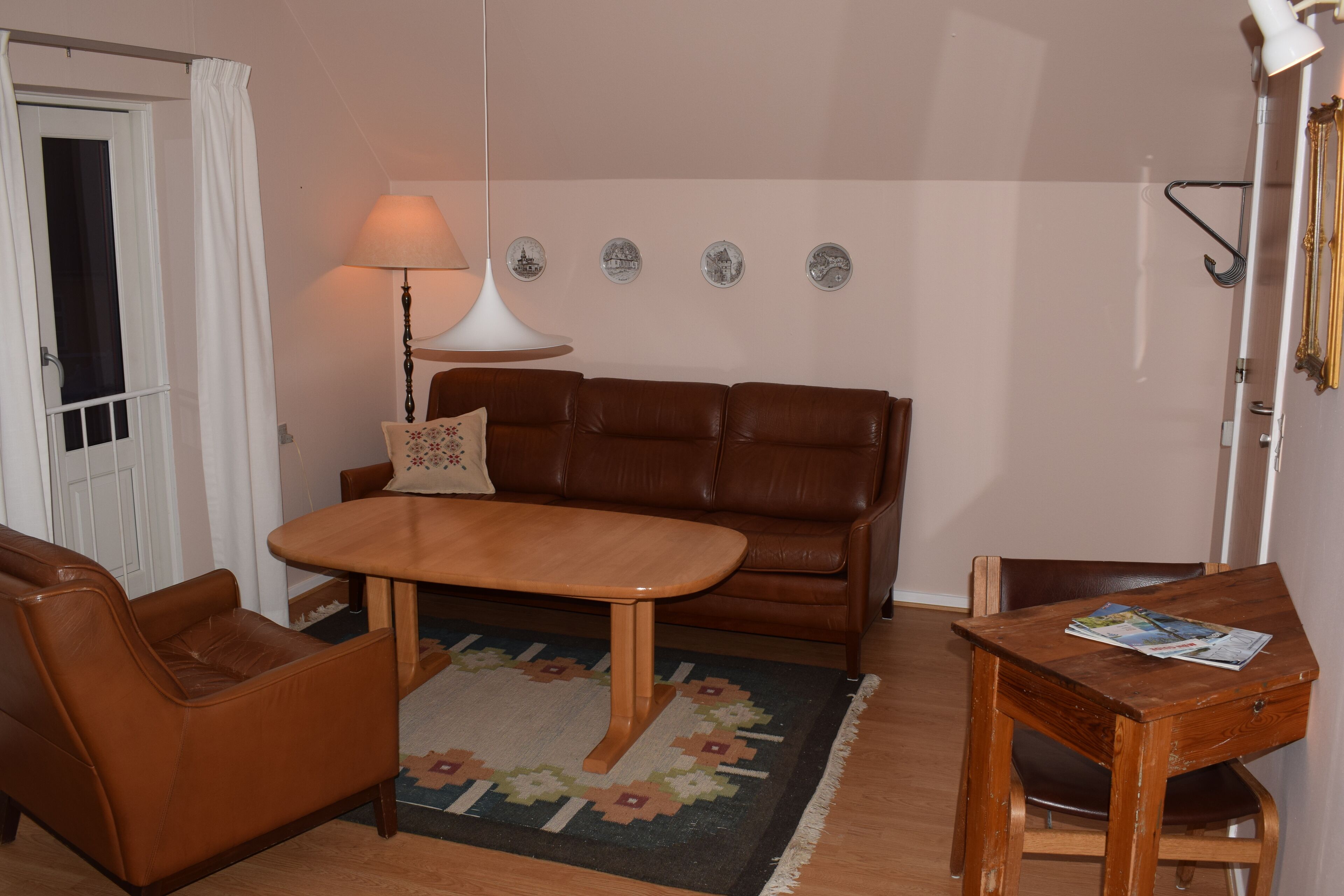 Un salón con un sofá de cuero marrón, una mesa de centro de madera y una mesita auxiliar con una revista.
