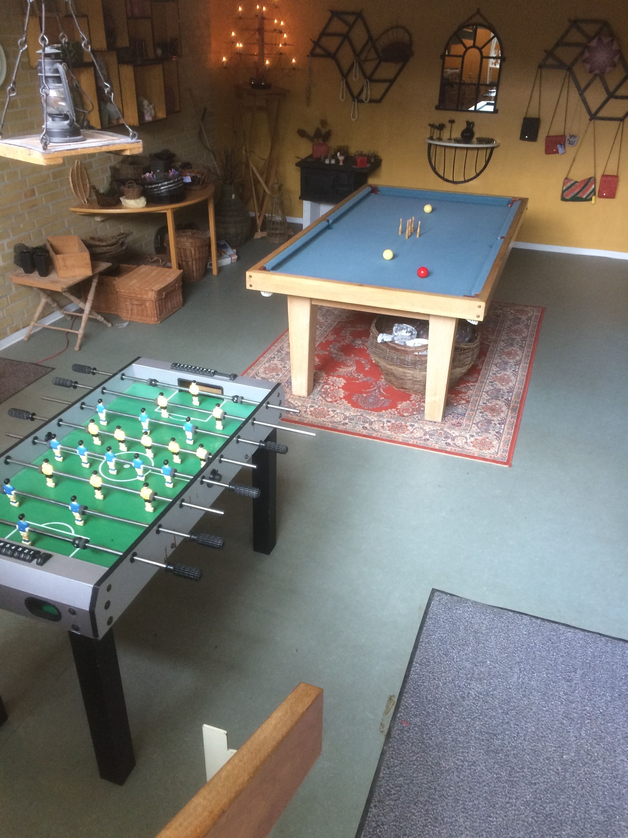 A room with a foosball table, a pool table, and a billiards table.