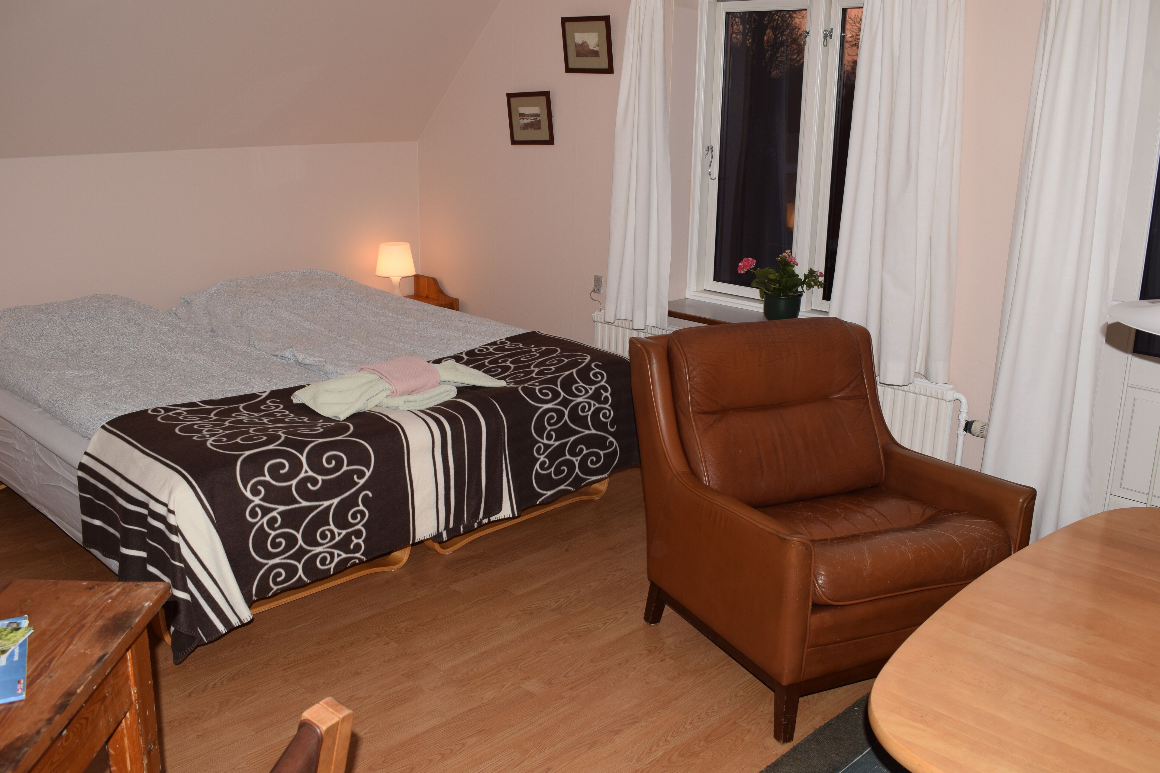 Une chambre à coucher avec un lit, un fauteuil en cuir marron, une table en bois et une fenêtre avec des rideaux.