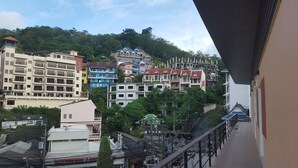 Un immeuble à plusieurs étages doté de balcons, d’un escalier et offrant une vue sur une colline parsemée de différents bâtiments.
