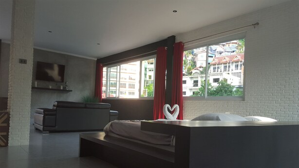Une chambre moderne avec un lit, un téléviseur fixé au mur et une grande fenêtre avec des rideaux.