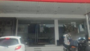 Un edificio con fachada roja y blanca, un acceso cubierto y un coche y una motocicleta estacionados al frente.