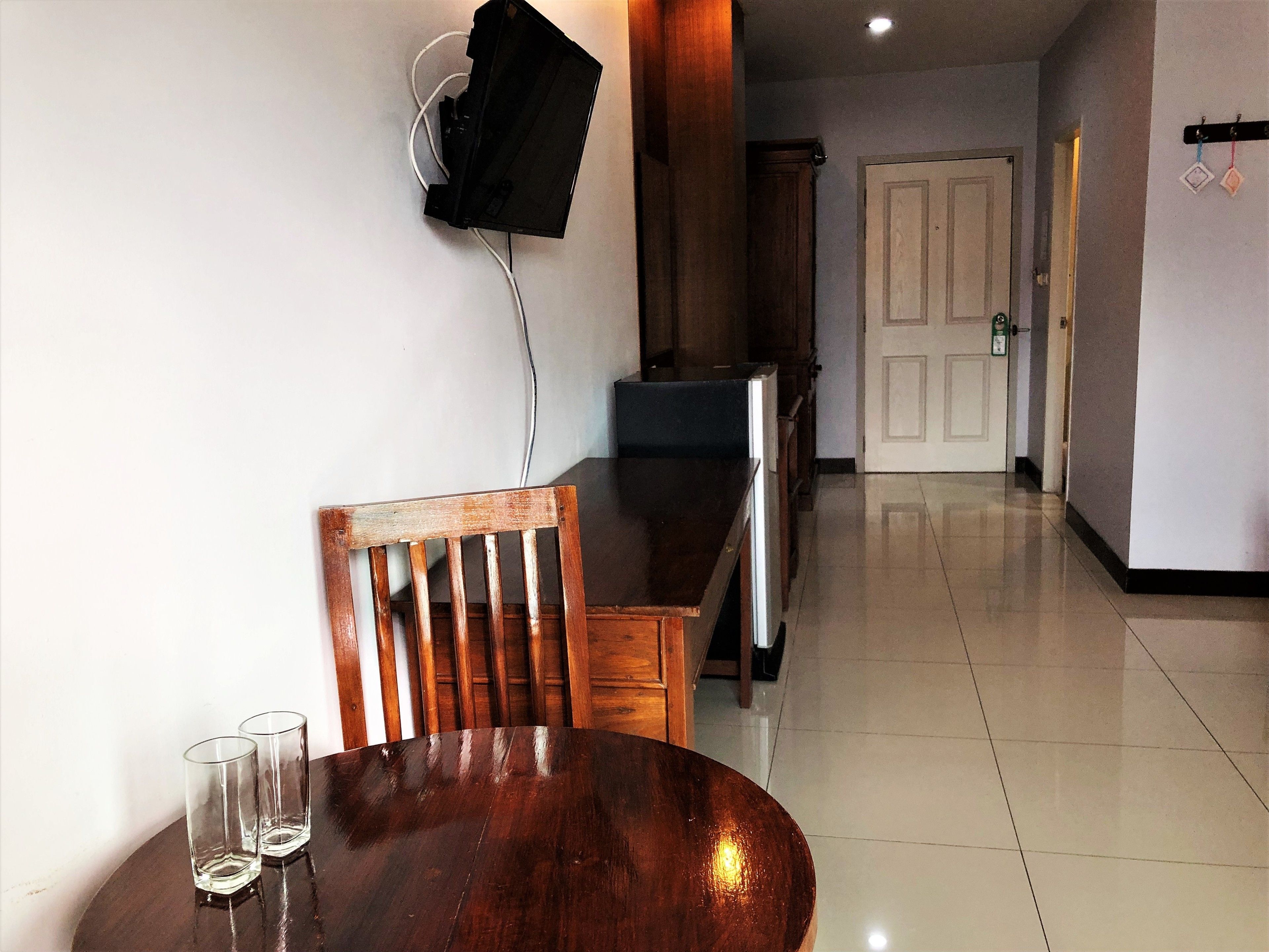 Un coin repas avec une table et des chaises en bois, un téléviseur fixé au mur et un couloir menant à une porte.