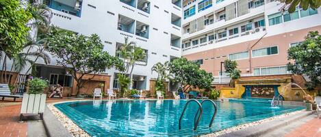 A swimming pool surrounded by a courtyard with a multi-story building, outdoor seating, and greenery.
