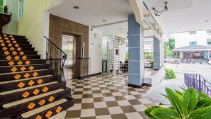 A hotel lobby with a checkered floor, a staircase with orange diamond patterns, and a view of the street outside. - Sutus Court 1 (Pattaya)