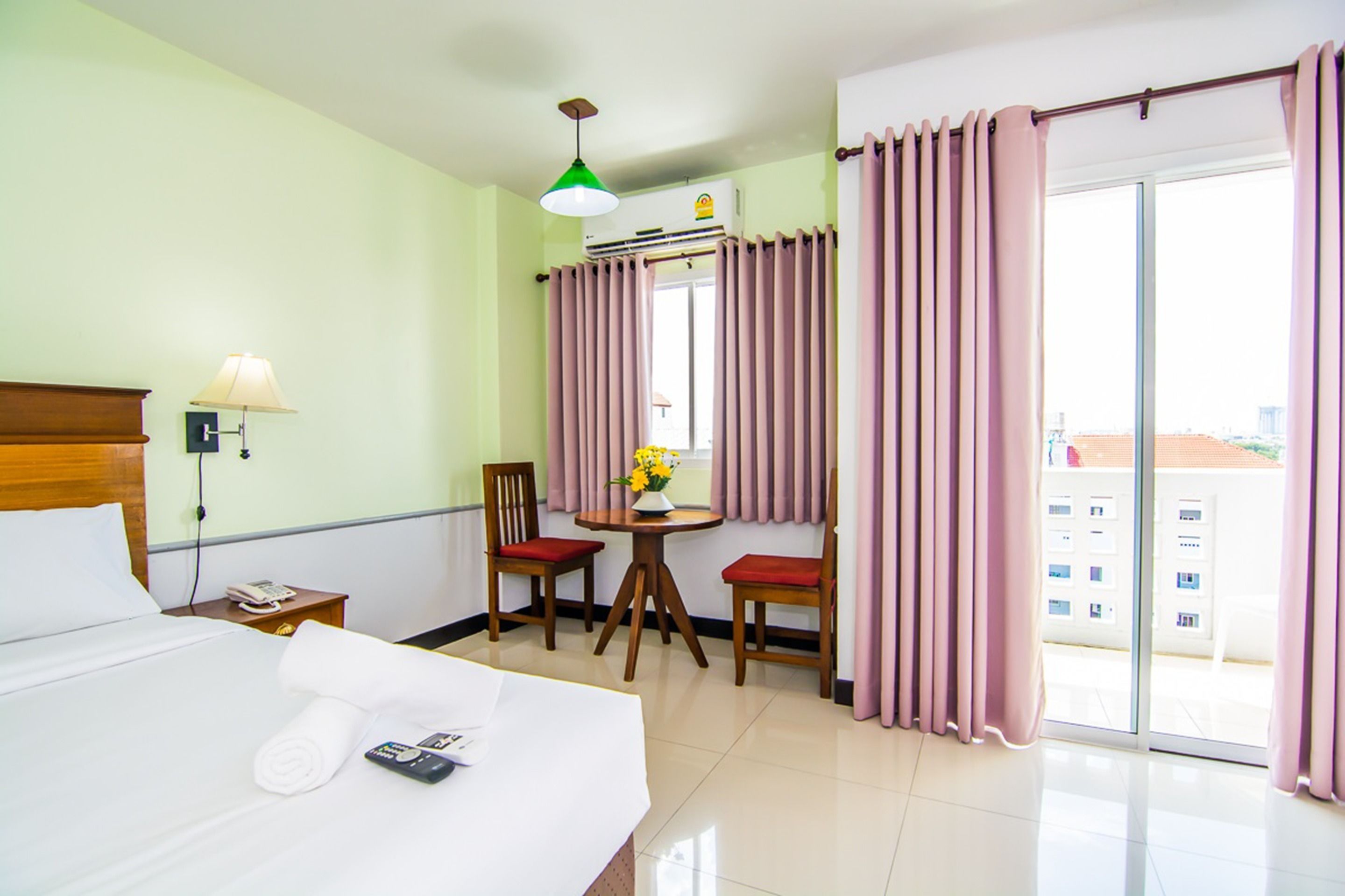A hotel room with a bed, a desk, two chairs, a table with flowers, a lamp, and a view through the window.