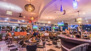 A modern bar area with wicker furniture, multiple TV screens, and hanging lights. - Sutus Court 1 (Pattaya)
