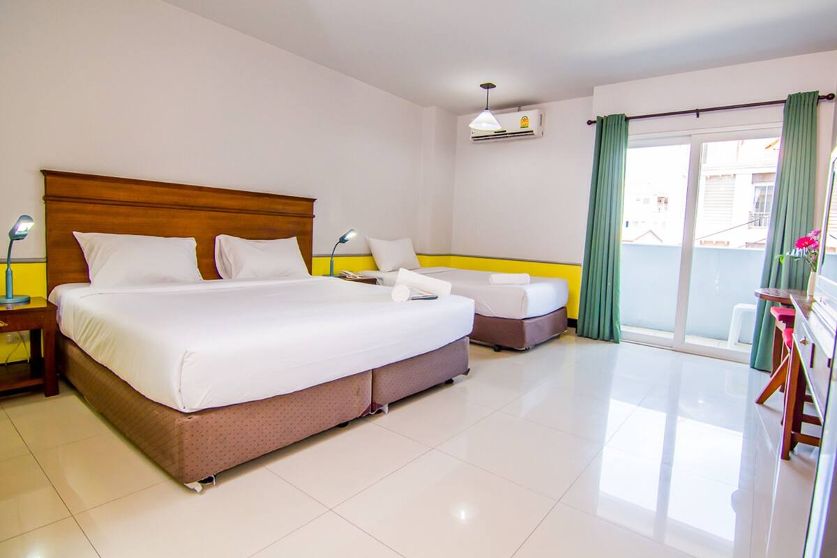 A hotel room with a large bed, a smaller bed, a desk, and a balcony with curtains.