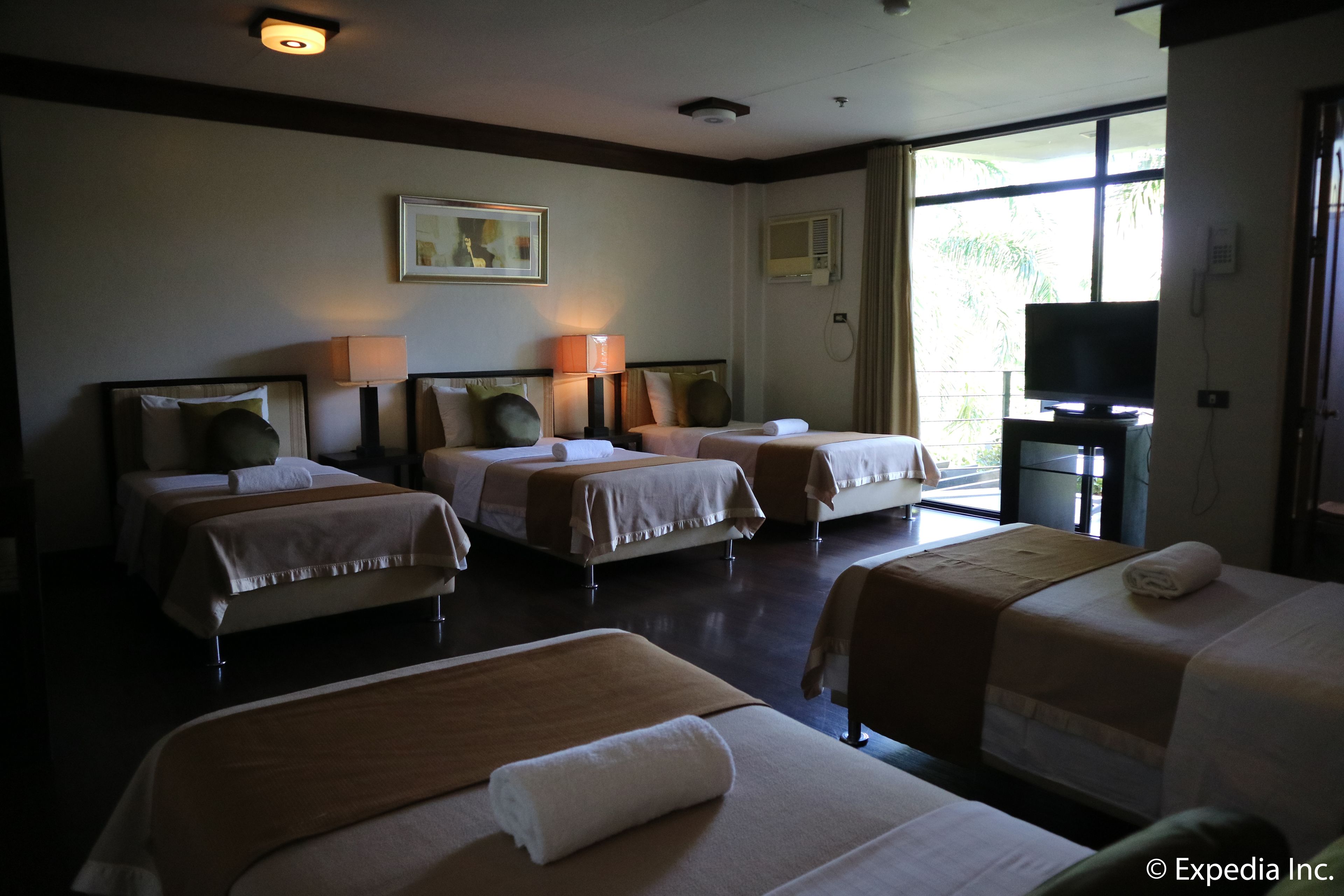 A hotel room with four beds, a television, and a large window with curtains.