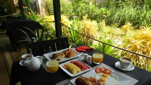 A breakfast table set outdoors with a variety of food items, including eggs, toast, and fruit, along with beverages and condiments. - Villa Nissa (Siem Reap)