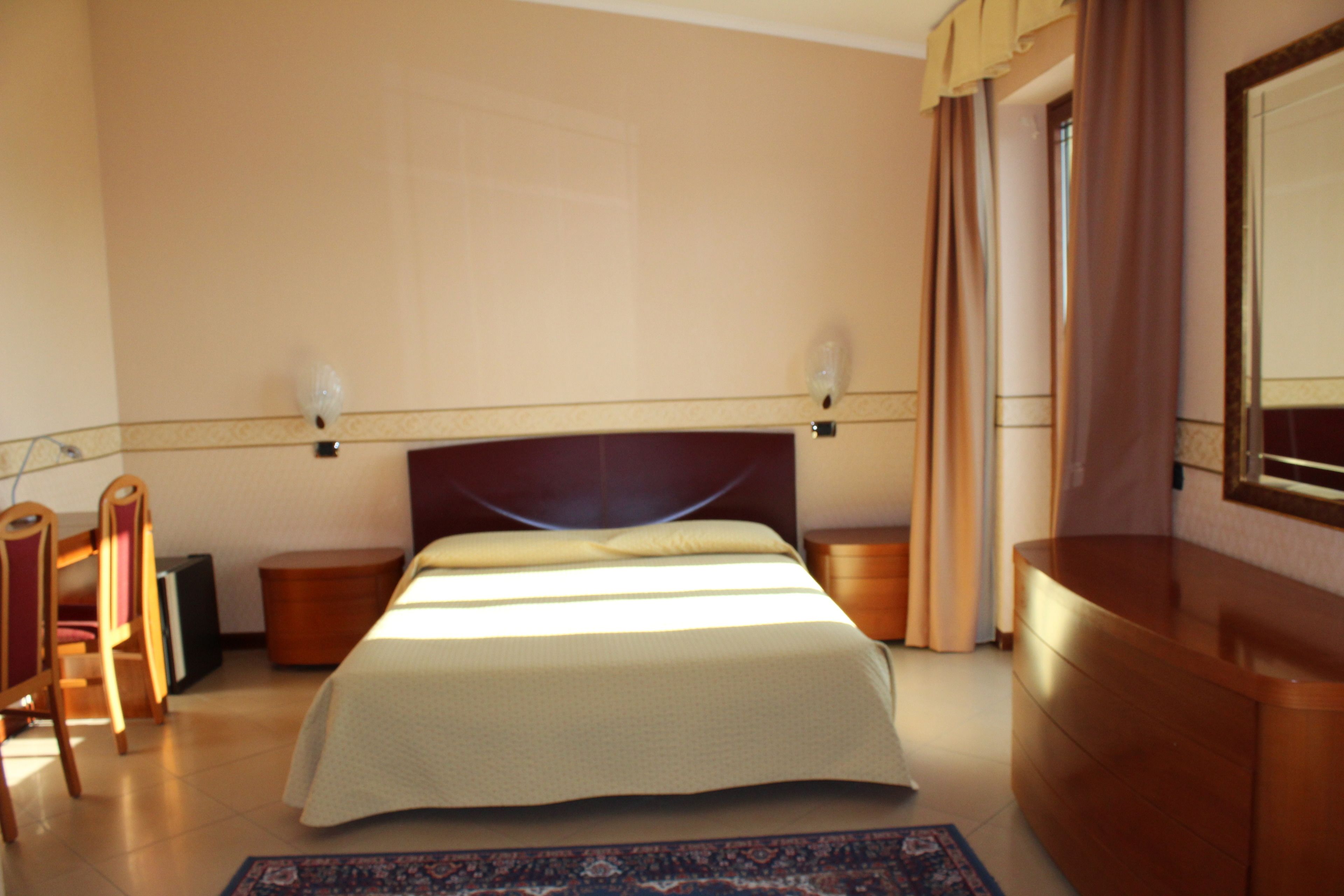 A hotel room with a large bed, wooden headboard, bedside tables, a desk, and a mirror.